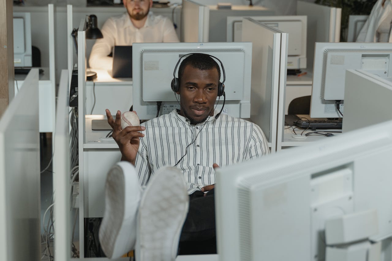 Man relaxing in office cubicle wearing headphones, holding a stress ball.