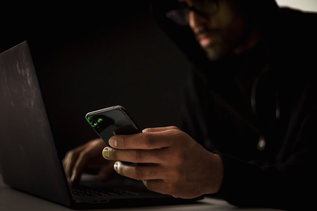 pexels photo 5935792 Crop anonymous ethnic male cyber spy with cellphone and netbook hacking system in evening